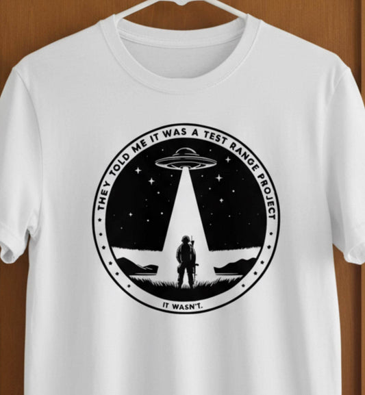 White t-shirt with a UFO and soldier graphic on a wooden door.