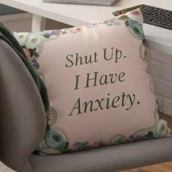 Decorative pillow with 'Shut Up. I Have Anxiety.' text on a chair in an office setting.