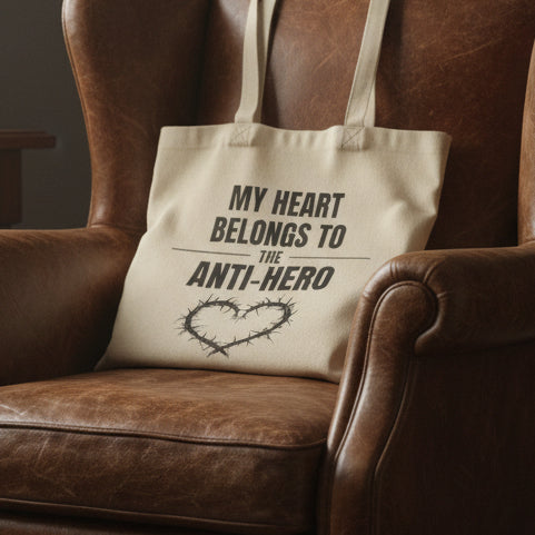 Beige tote bag with text 'My heart belongs to the anti-hero' on a white background