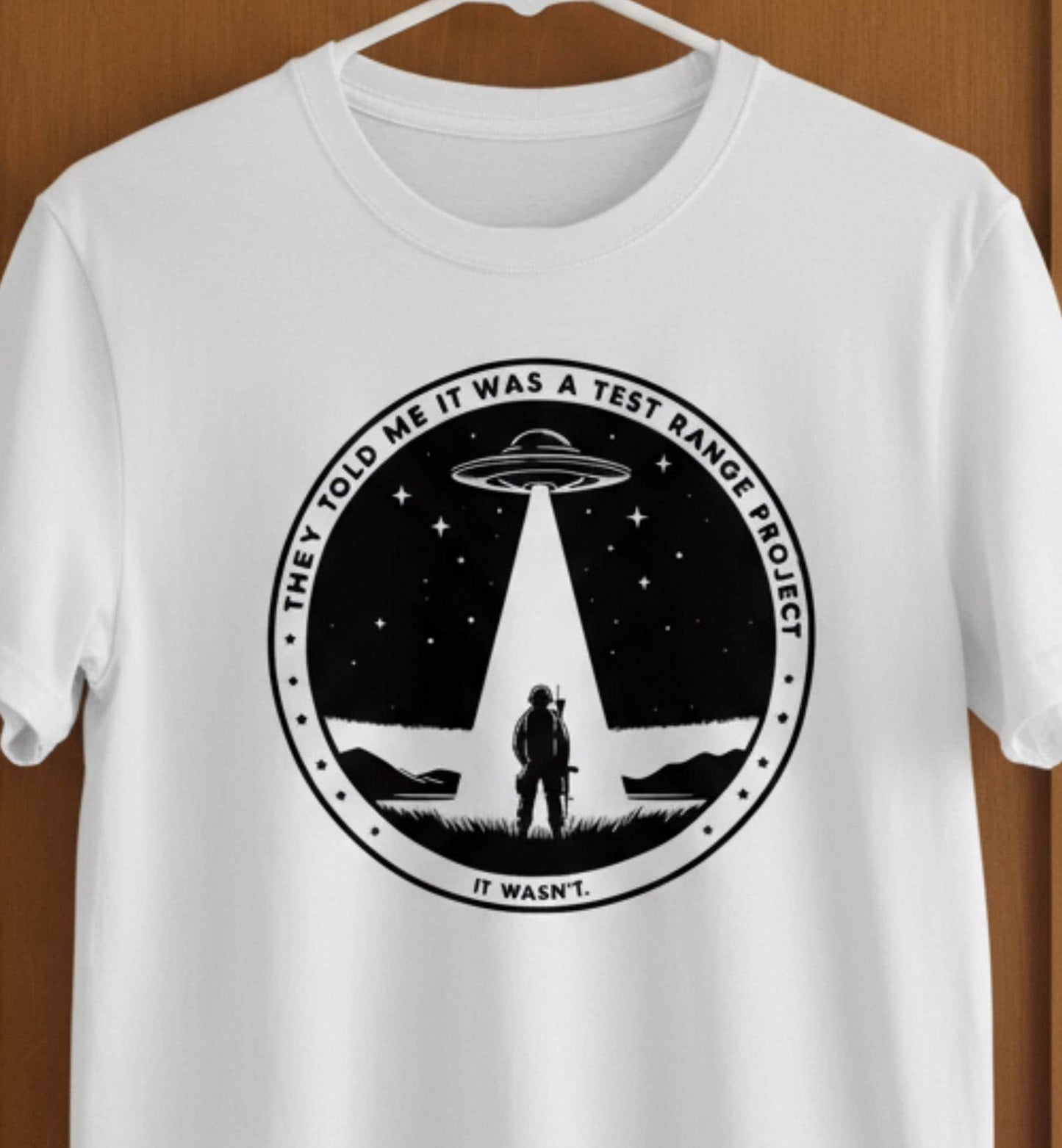 White t-shirt with a UFO and soldier graphic on a wooden door.